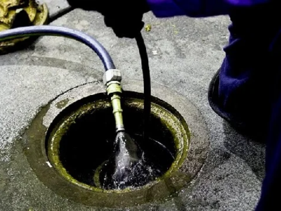 A professional plumber performing High Pressure Water Jetting to clear a commercial sewer line through an open access manhole.