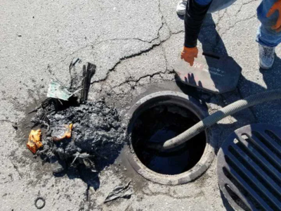 An emergency plumber in Fort Lauderdale uses a high-powered vacuum hose to clear a massive sewage backup and debris from an open outdoor manhole.