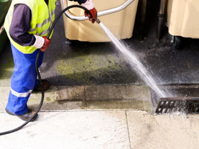 A technician in a high-visibility safety vest performing emergency High Pressure Water Jetting to clear a clogged storm drain.