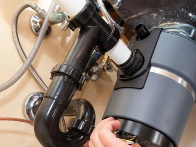 Professional plumber performing a garbage disposals install in Fort Lauderdale, focusing on the electrical wiring and secure mounting of a new unit under a kitchen sink.