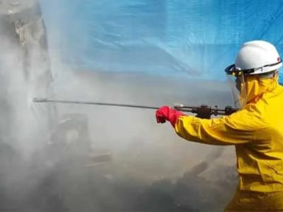 A technician in a yellow safety suit and face shield performing High Pressure Water Jetting for a Sewer Line Inspection and preventative maintenance.