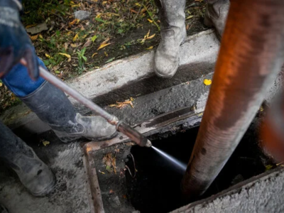A plumbing specialist performing high pressure water jetting into an open sewer access point to clear debris and blockages.
