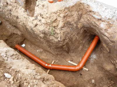 A professional sewer line repair in Fort Lauderdale featuring new orange PVC piping installed in a deep outdoor trench.