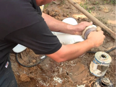 Professional plumber performing a sewer line repair in Fort Lauderdale, applying sealant to white PVC piping in an outdoor trench.