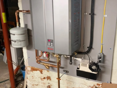 A grey Rinnai tankless water heater mounted on a wall with copper piping, a small white thermal expansion tank, and a black and white condensate neutralizer pump unit below it.